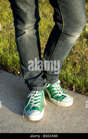 Ein Mädchen im Teenageralter Beine tragen dünne blaue Denimjeans und grüne Converse Sneakers für ihre Füße Stockfoto