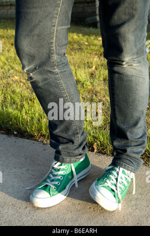 Ein Mädchen im Teenageralter Beine tragen dünne blaue Denimjeans und grüne Converse Sneakers für ihre Füße Stockfoto
