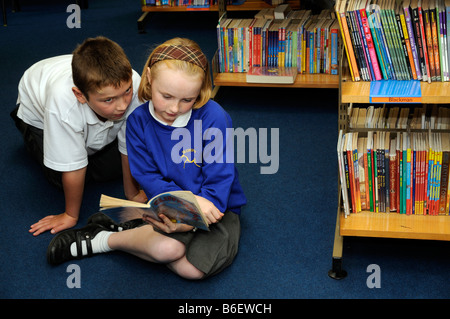 Kinder-Bibliothek Schüler lesen ein Buch ausgewählt aus den Regalen Stockfoto