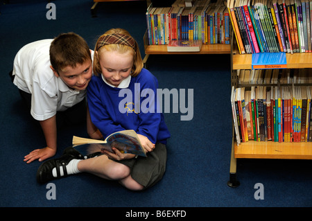 Kinder-Bibliothek Schüler lesen ein Buch ausgewählt aus den Regalen Stockfoto