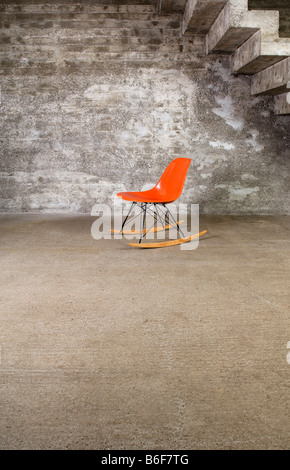 Orange Designer Schaukelstuhl in einem leeren Raum vor einer Betonwand Stockfoto