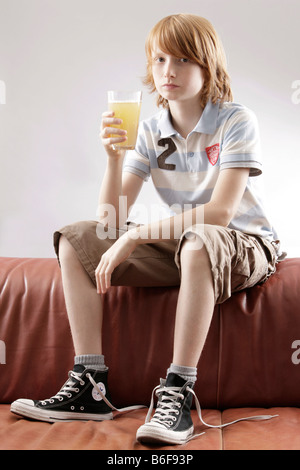 12 jähriger Junge, sitzt auf einem Sofa mit einem Glas Saft Stockfoto