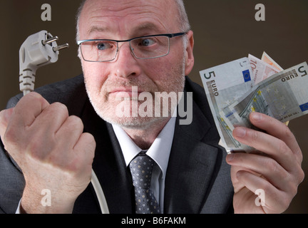 Mann hält eine elektrische Stecker und Banknoten, teuren Strom Stockfoto