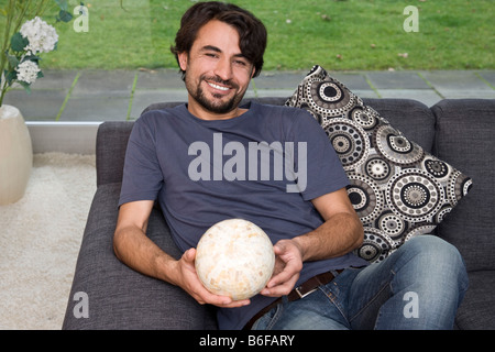 Mann sitzt auf einem Sofa strahlt, eine Glaskugel in den Händen hält Stockfoto