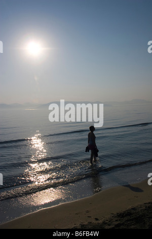 Hinterleuchtete junge Frau zu Fuß am Strand Stockfoto