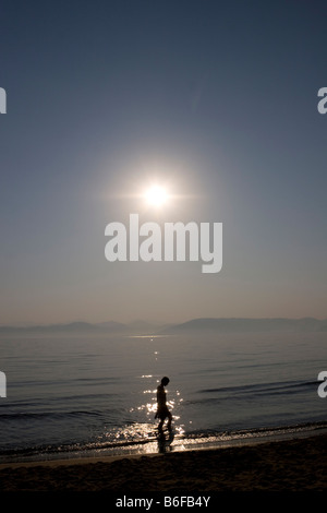 Hinterleuchtete junge Frau zu Fuß am Strand Stockfoto