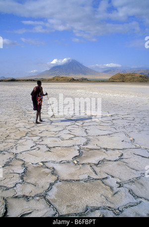 Maasai warrier ist zu Fuß auf dem Dired-Out Natron-See genannt Natron-See im Norden von Tansania, im Hintergrund die Heilige Hütte Stockfoto