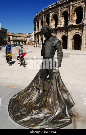 Radfahrer hinter die Bronzestatue der Bull Fighter Christian Montcouquiol, El Nimeno II, vor der Arena, die Nimes ein Stockfoto