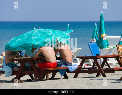 Vier Männer unter einem Sonnenschirm, Lady's Mile Beach, in der Nähe von Limassol, Südzypern, Europa Stockfoto
