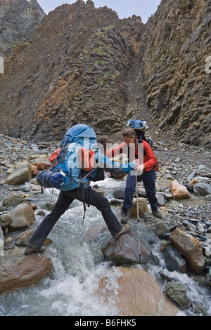 Zwei Wanderer, Rucksacktouristen, Frauen, Kreuzung Creek, helfen, Donjek Route, St. Elias Mountains, Kluane National Park, Yukon te Stockfoto