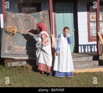 Eine Mutterfigur schlägt den Staub aus Teppichen, während ein junges Mädchen ihre Nase hält Stockfoto