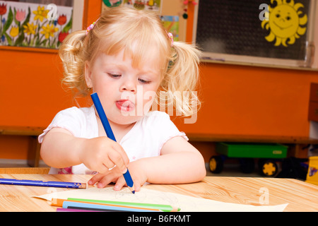 Blondes Mädchen, 3 Jahre, mit Buntstiften am Tisch sitzen Stockfoto