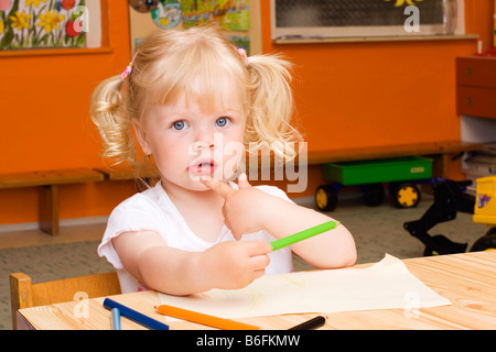 Blondes Mädchen, 3 Jahre, mit Buntstiften am Tisch sitzen Stockfoto