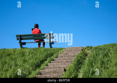 Frau sitzt in Bank am Deich Niederlande Stockfoto