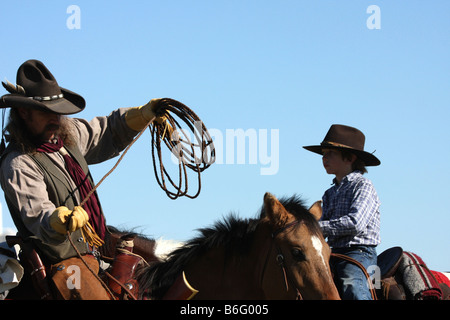 Ein Cowboy-Vater auf dem Pferderücken zeigt seinen Sohn wie ein Seil, um Vieh zu fangen zu werfen Stockfoto