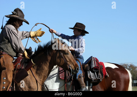 Ein Cowboy-Vater auf dem Pferderücken zeigt seinen Sohn wie ein Seil, um Vieh zu fangen zu werfen Stockfoto