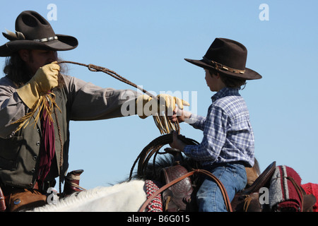 Ein Cowboy-Vater auf dem Pferderücken zeigt seinen Sohn wie ein Seil um Rinder Abseilen Lasso fangen zu werfen Stockfoto