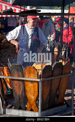 Senior man bereitet langsam gekochte Lachsfilets mit offenem Feuer im Freien auf der Kalaryssäys Kalaryssaeys Fischmarktmesse in Kuopio City Finland zu Stockfoto