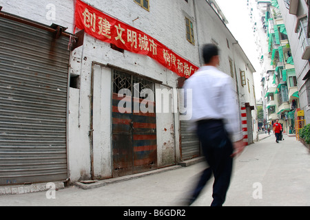 Chinesen, die zu Fuß durch städtische Seitenstraßen des alten Kantons vorbei an alten Lagerhalle im Wohnviertel unter propaganda Stockfoto