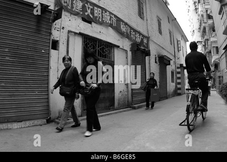 Chinesen, die zu Fuß durch städtische Seitenstraßen des alten Kantons vorbei an alten Lagerhalle im Wohnviertel unter propaganda Stockfoto