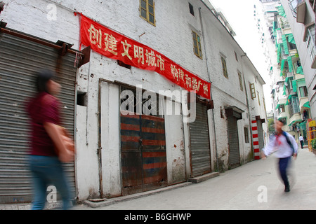 Chinesen, die zu Fuß durch städtische Seitenstraßen des alten Kantons vorbei an alten Lagerhalle im Wohnviertel unter propaganda Stockfoto