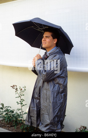 Hispanic Mann im Regenmantel schützt sich vor Regen mit Regenschirm Stockfoto