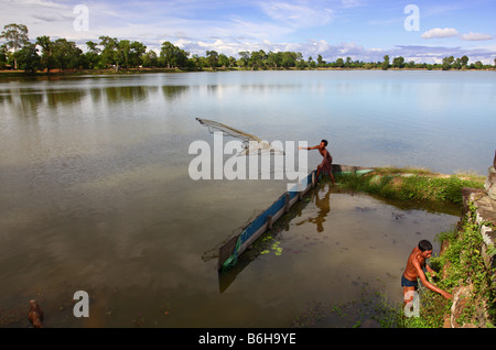 Lokale Fischer sein Netz in einem großen Teich in der Nähe von Angkor Wat komplex und andererseits Kommissionierung einige Wildgemüse auswarf Stockfoto