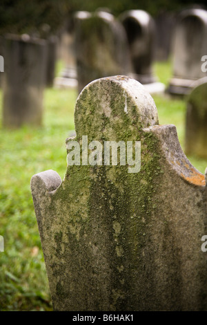 Detail einer alten krummen getragen frühen amerikanischen Grabstein bedeckt mit Moos und Flechten, anderen Steinen im Hintergrund sichtbar. Stockfoto