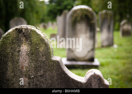 Detail des oberen Teils eines alten frühen amerikanischen Grabstein mit Jahre im Wert von Verschleiß, Flechten und Moos, andere Grabsteine sichtbar hinter. Stockfoto