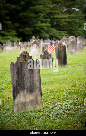 Alte amerikanische Friedhof aus dem 18. und 19. Jahrhundert Ära Grabsteine, eine amerikanische Flagge markiert ein Veteranen-Grab im Hintergrund. Stockfoto