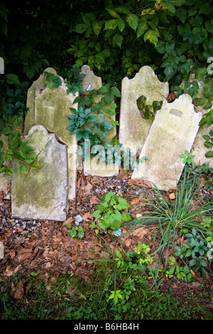 Verworfen/aufgegeben und zerbrochene Grabsteine entlang einer alten Steinmauer mit üppigem grün bewachsenen aufgetürmt. Stockfoto