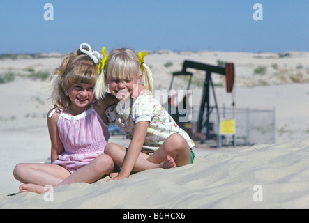 Zwei junge Schwestern spielen in den Sanddünen in der Nähe eine pumpende Ölquelle in den Panhandle von West Texas in der Nähe von Odessa Stockfoto