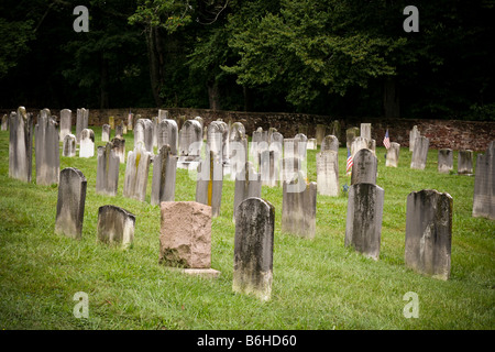 Eine alte frühen amerikanischen Kirche Friedhof mit Reihen von einfachen Marmor Grabsteine, einer Steinmauer und Bäume im Hintergrund. Stockfoto