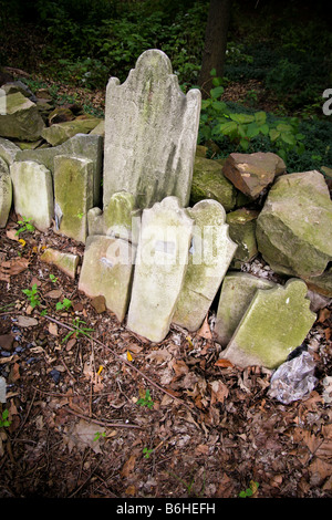 Alte ausrangierte, abgenutzte und gebrochene Grabsteinen gestapelt gegen eine Steinmauer mit dichten grünen und Laub überwuchert. Stockfoto