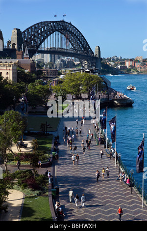 Die Menschen gehen entlang des Hafens von Sydney in The Rocks, mit der Sydney Harbour Bridge im Hintergrund, Sydney, New South Wales Stockfoto