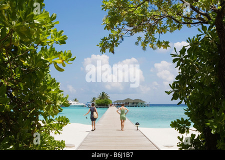 Zwei junge Frauen, die zu Fuß hinunter in Richtung Hafen auf einer Insel in den Malediven Stockfoto