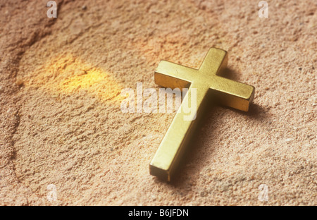 Nahaufnahme eines einfachen gold Kruzifix auf grobe rosa Steinoberfläche mit zwei goldenen Keile Licht projiziert in der Nähe liegen Stockfoto