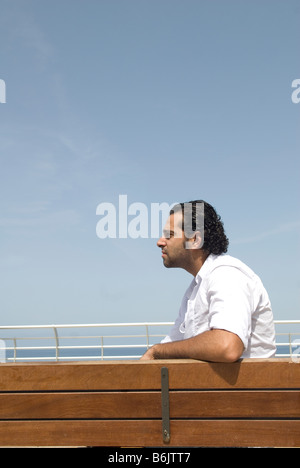 Junger Mann sitzt auf der Bank am Meer Stockfoto