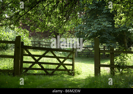 Summer view of open gate, post and rail fencing green dappled sunlight Stockfoto