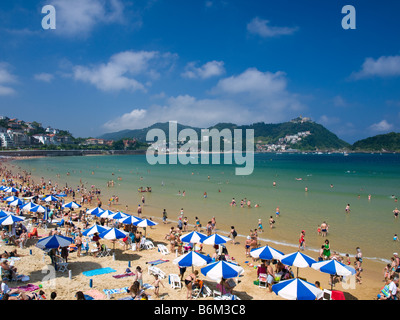 Strandliebhaber schlagen die Playa De La Concha in San Sebastián, Spanien an einem heißen Sommertag. Stockfoto