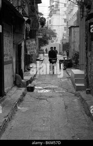 Mann Reiten Fahrrad allein an den ersten kalten Morgen im Jahr morgens eine Seitenstraße Gasse in Guangzhou China Black und Stockfoto