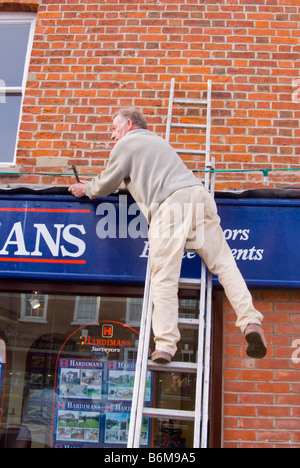 Mann Reparatur Blei blinken über einem Ladenschild Shop arbeiten von einer Leiter in Großbritannien Stockfoto