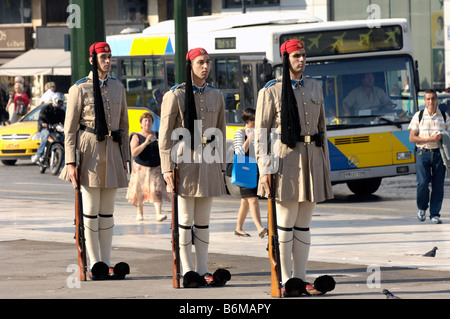 Drei Evzones warten, während die Wachablösung mit dem Transport von Athen hinter ihnen - die Veranstaltung findet in der Öffentlichkeit. Stockfoto