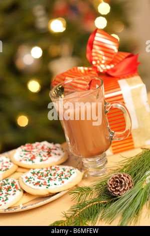 Festliche Szene mit Glas heißer Kakao Teller mit Plätzchen und Weihnachtsgeschenk mit beleuchteten Weihnachtsbaum im Hintergrund. Stockfoto