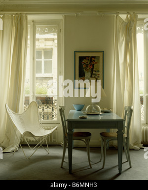 Weiße Leinwand Butterly Stuhl und blass blauen Tisch und Stühle im Stadthaus Speisesaal mit cremefarbenen Vorhängen an französischen Fenstern Stockfoto