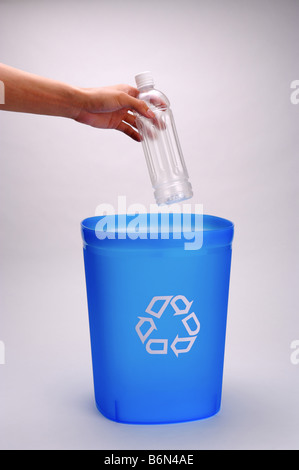 Junger Mann s Hand hält eine Leere Plastikflasche über eine blaue Recyclingbehälter Stockfoto