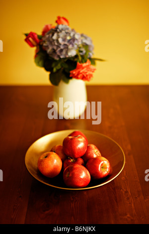 Schale von Äpfeln auf Tisch mit Vase mit Blumen Rosen und Hortensien Stockfoto