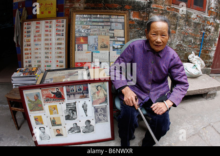 Eine sehr nette schöne und elegante chinesische Dame im Alter von 93 Jahren sitzt vor ihrem Buchladen in Guangzhou mit Mao-Propaganda. Stockfoto