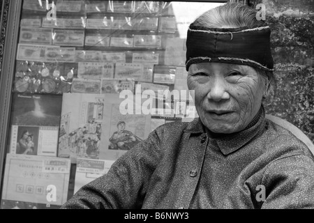 Eine sehr nette schöne und elegante chinesische Dame im Alter von 93 Jahren sitzt vor ihrem Buchladen in Guangzhou mit Mao-Propaganda. Stockfoto