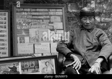 Eine sehr nette schöne und elegante chinesische Dame im Alter von 93 Jahren sitzt vor ihrem Buchladen in Guangzhou mit Mao-Propaganda. Stockfoto